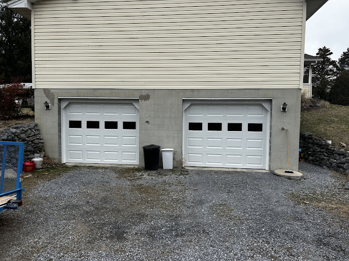 Two white garage doors on beige siding with gravel driveway