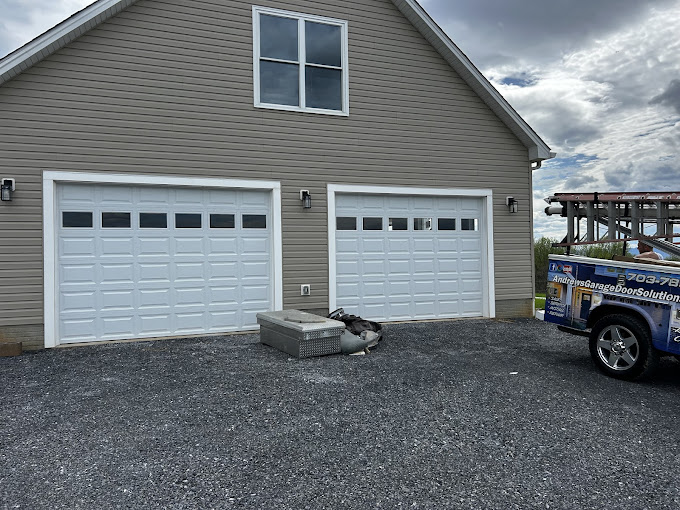 Two-car garage with white doors and service truck parked on gravel