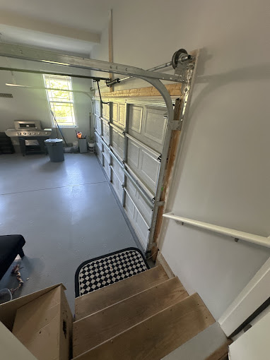 Open garage door with stairs, leading to interior workspace with tools