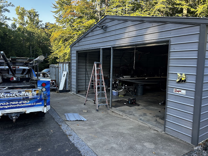 Gray metal workshop with open door, ladder, and work trailer outside
