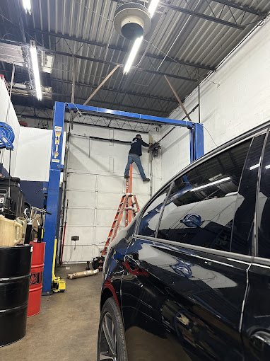 Worker on ladder repairs automotive lift in car repair garage