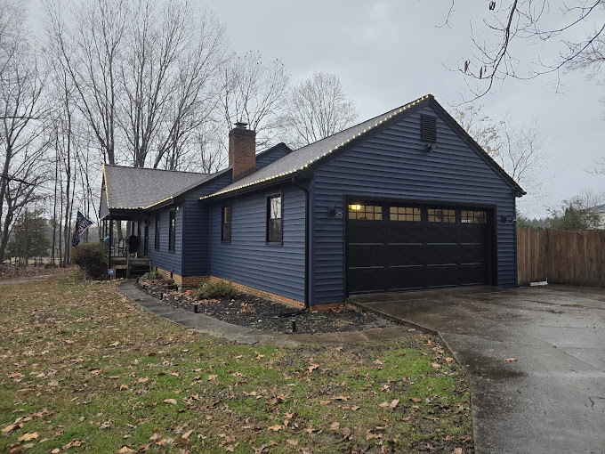 Blue house with attached garage on a leafy lot during winter